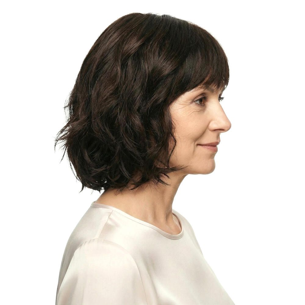 Perücke Capri, braun, gewellt. Frau im Profil, Blick nach rechts. Helles Oberteil.