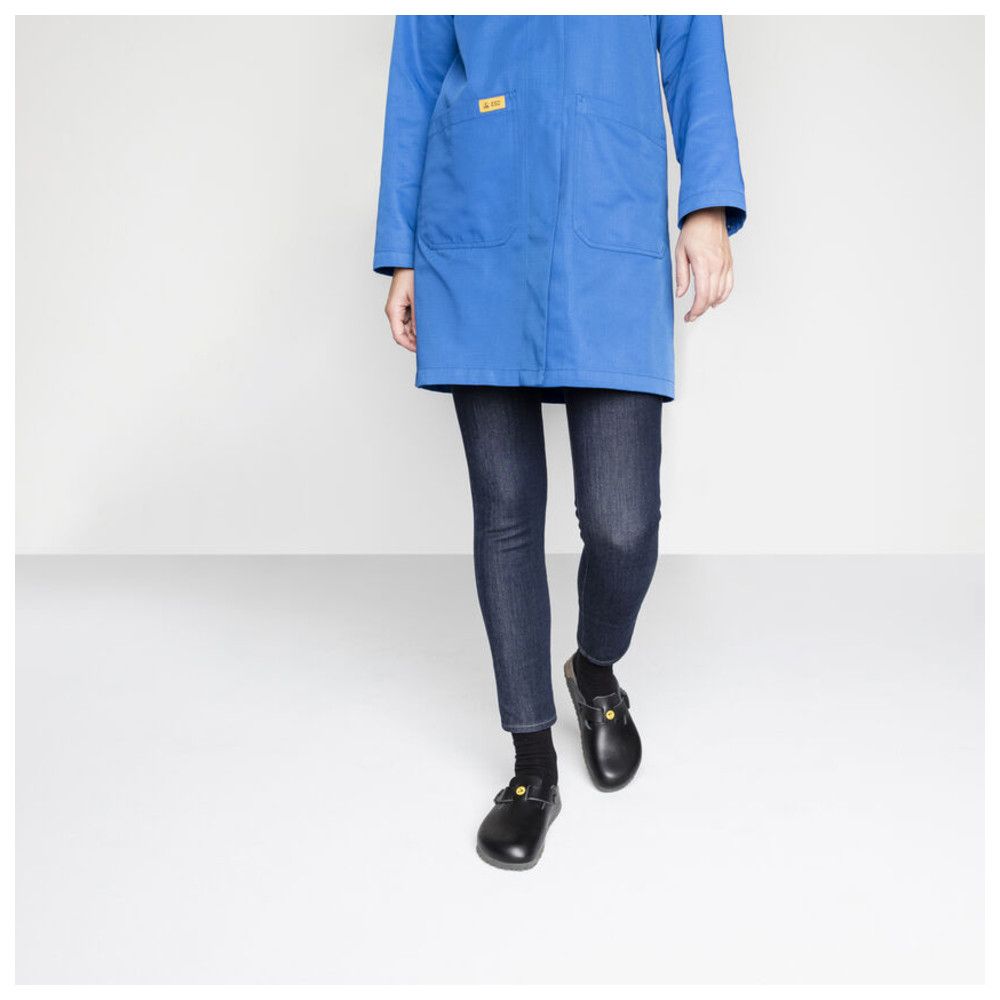 Person trägt schwarze Pantoletten. Blaue Arbeitskleidung, Jeans. Gelbes ESD-Logo an den Schuhen.