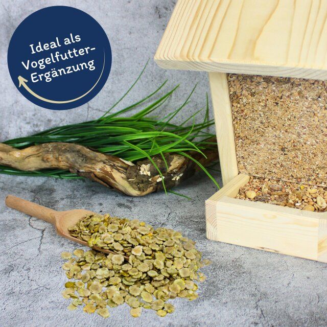 Erbsenflocken neben Vogelhaus. Beschriftung: Ideal als Vogelfutter-Ergänzung. Holzschaufel. Holzhaus mit Futter.