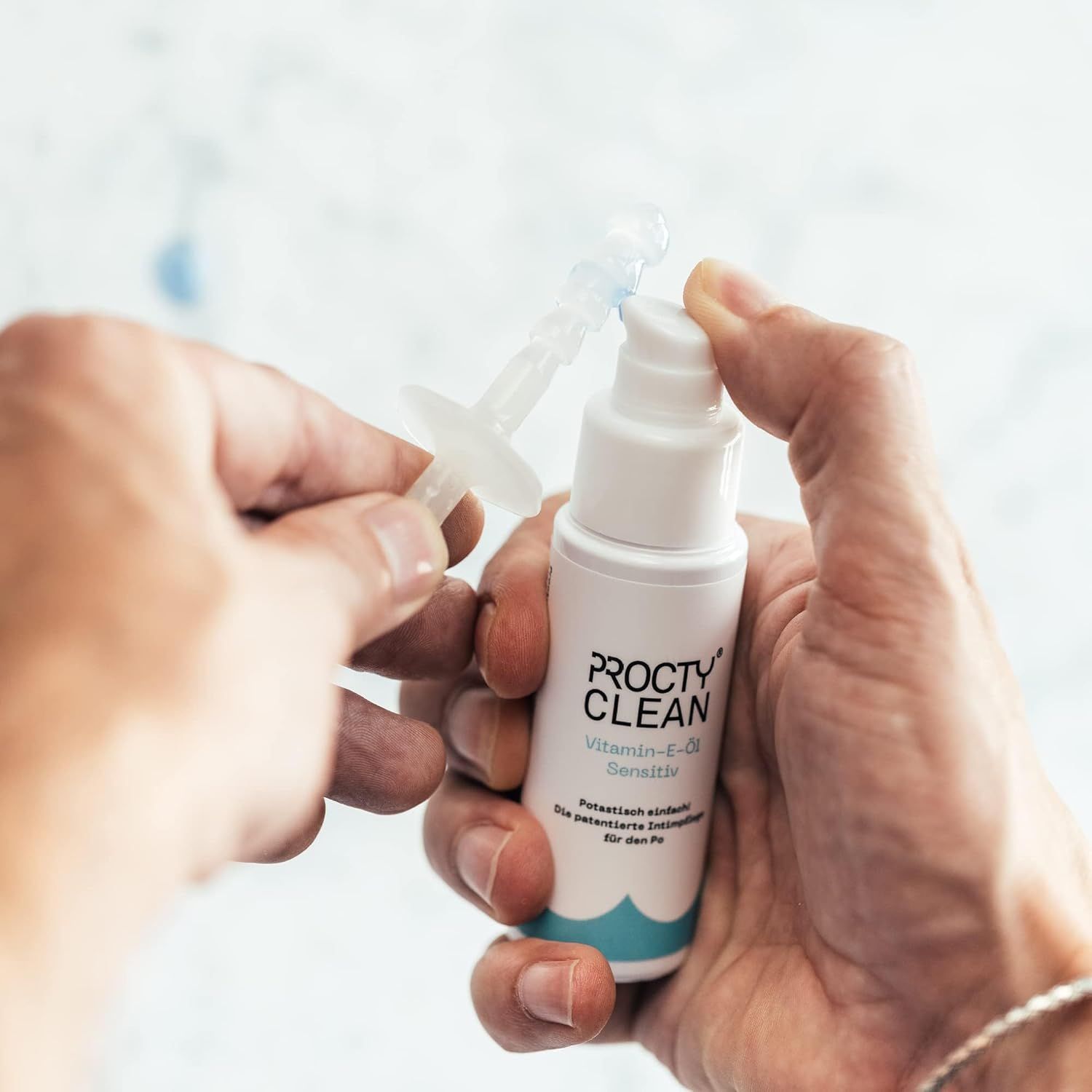 Person hält ProctyClean Vitamin-E-Öl Sensitiv Flasche und Applikator. Weißer Hintergrund.