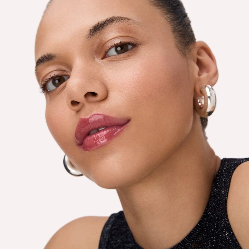 Porträt einer Frau mit glänzendem Lip Balm. Sie trägt Ohrringe.