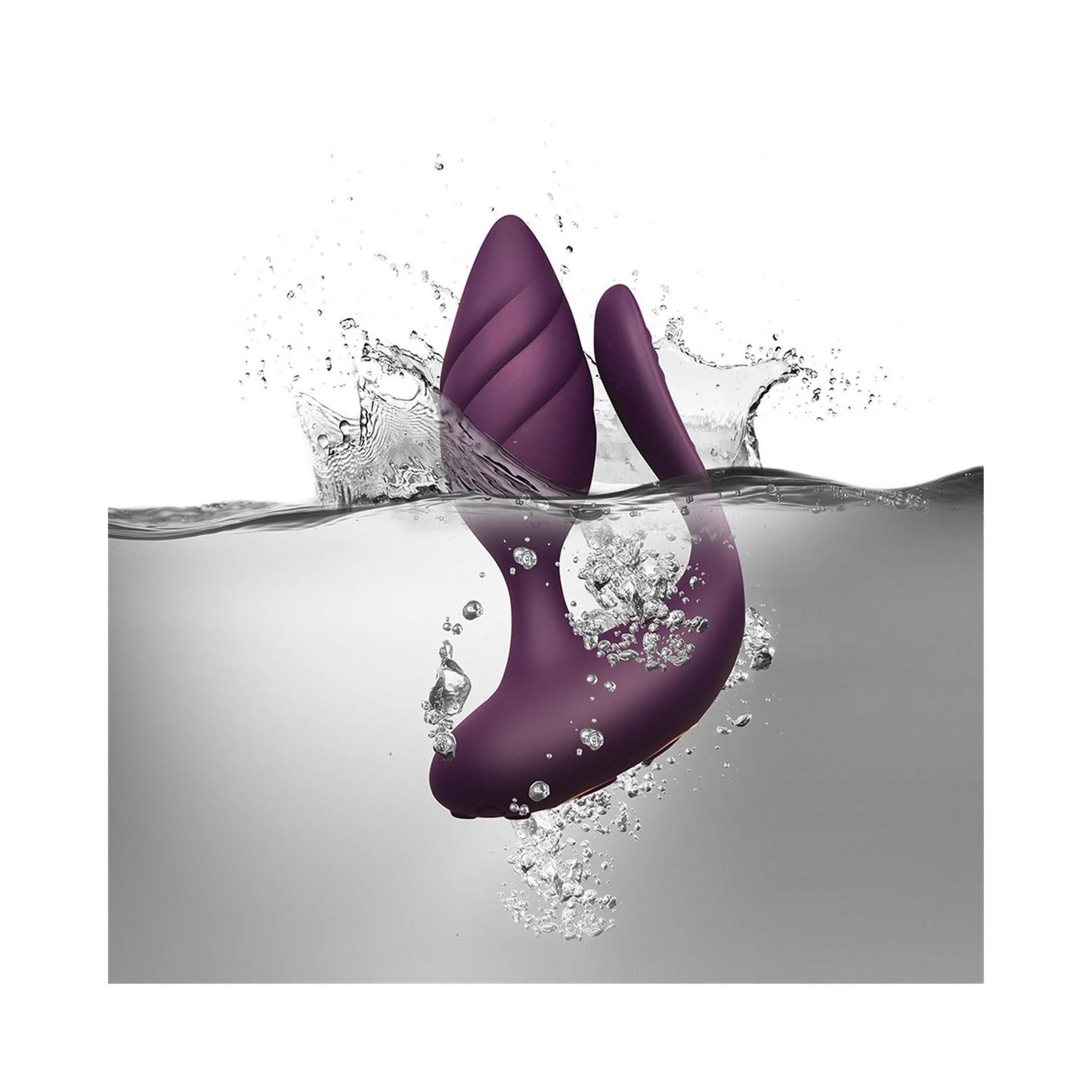 Lila Wellness-Produkt im Wasser. Geriffelte Spitze, geschwungene Form. Wasser spritzt. Produkt untergetaucht.