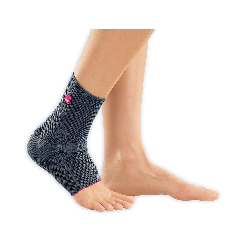 Knöchelbandage Medi Levamed®. Anthrazitfarbenes Gestrick mit pinkfarbenen Akzenten. Logo auf der Außenseite. Am Fuß einer Person getragen.