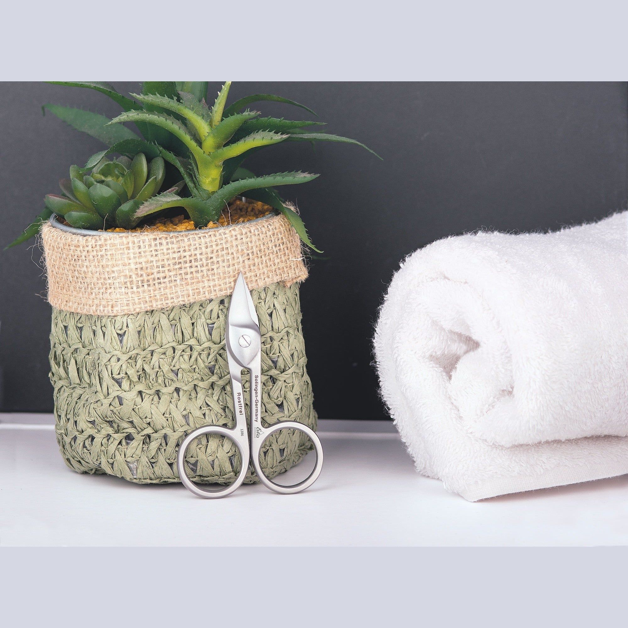 Nagelschere neben einem Handtuch und einem Topf mit Pflanze. Produktpräsentation. Hintergrund: schwarz und weiß.