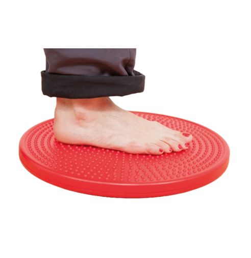 Roter Therapiekreisel mit Noppen, Fuß darauf. Person trägt dunkle Hose.