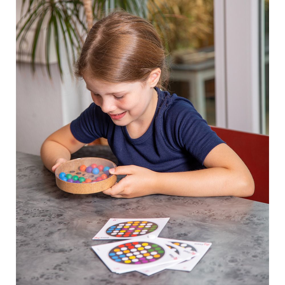 Kind hält ein Spiel mit bunten Kugeln und Karten. Das Spiel hat eine runde Form mit Löchern und einer transparenten Abdeckung.