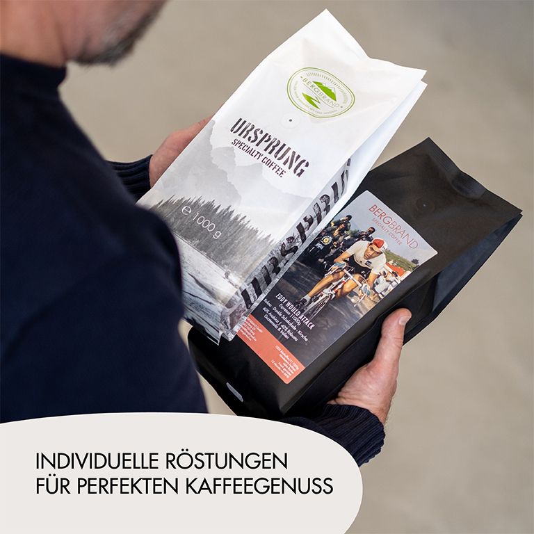 Zwei Kaffeebohnen-Packungen. Eine mit Text Ursprung, eine mit Radfahrer-Motiv. Person hält sie.