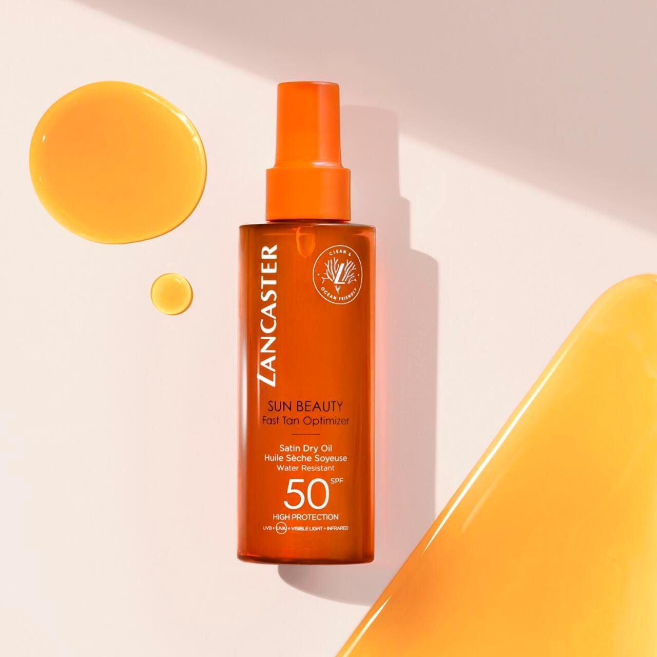 Lancaster Sun Beauty Dry Oil Fast Tan Optimizer SPF50. Eine transparente Flasche mit orangefarbenem Öl und Sprühkopf. Daneben befinden sich Öltropfen. Der Hintergrund ist hell.