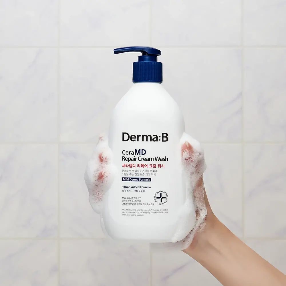 Weiße Flasche mit blauem Pumpkopf in einer Hand. Schaum. Aufschrift: Derma:B CeraMD Repair Cream Wash. Hintergrund: Kacheln.