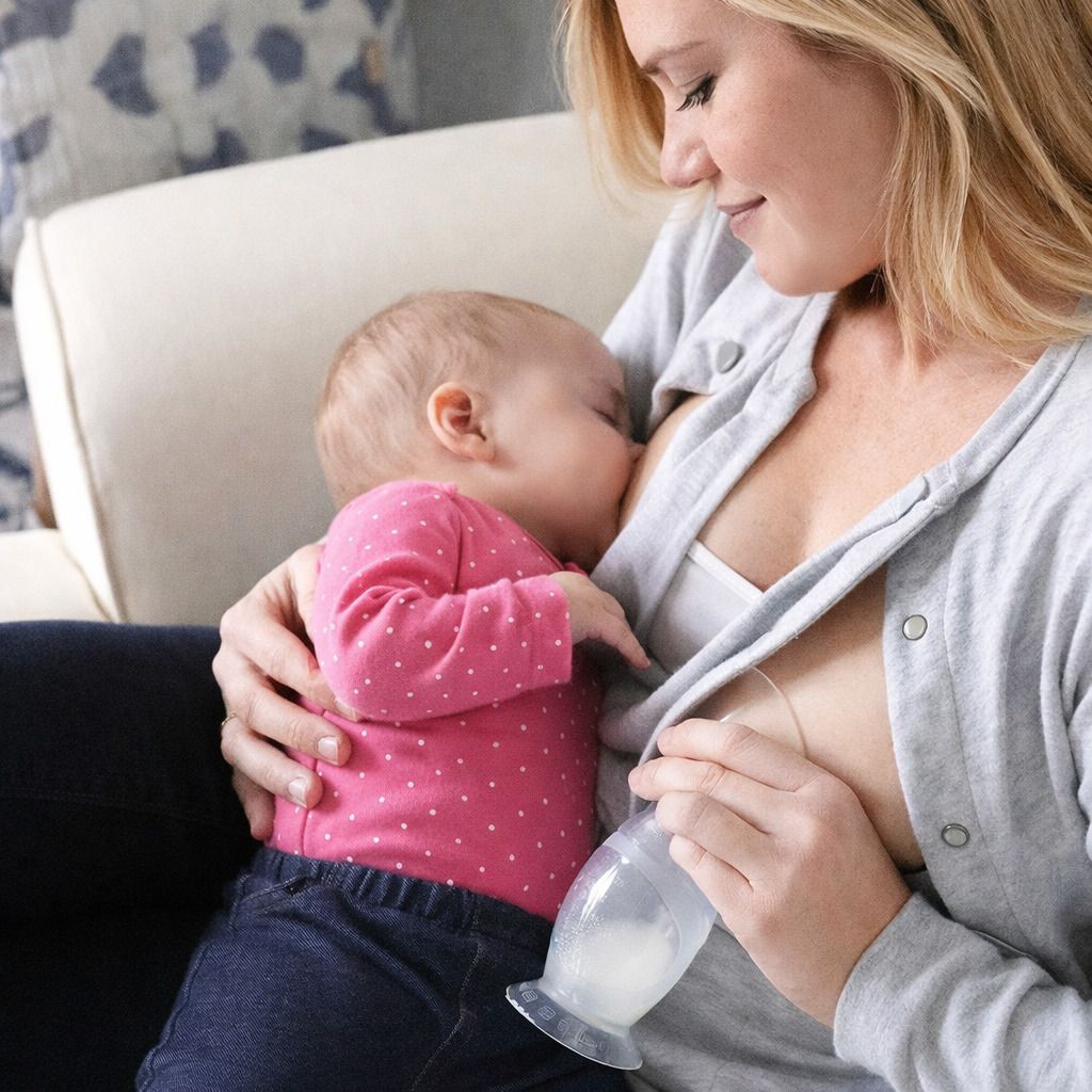 Frau stillt Baby mit Milchpumpe. Baby trinkt an der Brust, Milchpumpe am anderen. Frau sitzt.