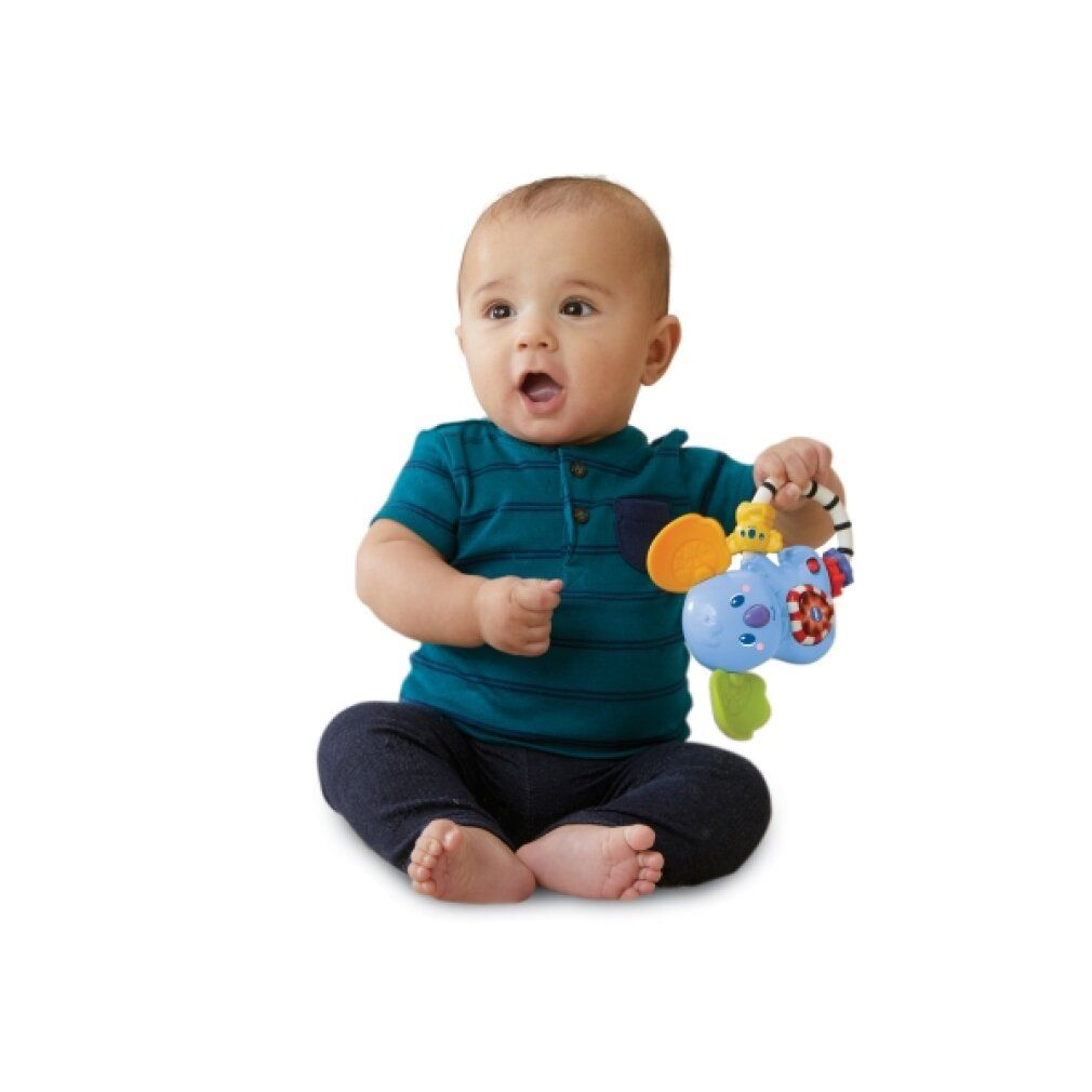 Baby sitzt und hält blaues Koala-Rasselspielzeug. Ring mit bunten Ringen und einem gelben Koala.