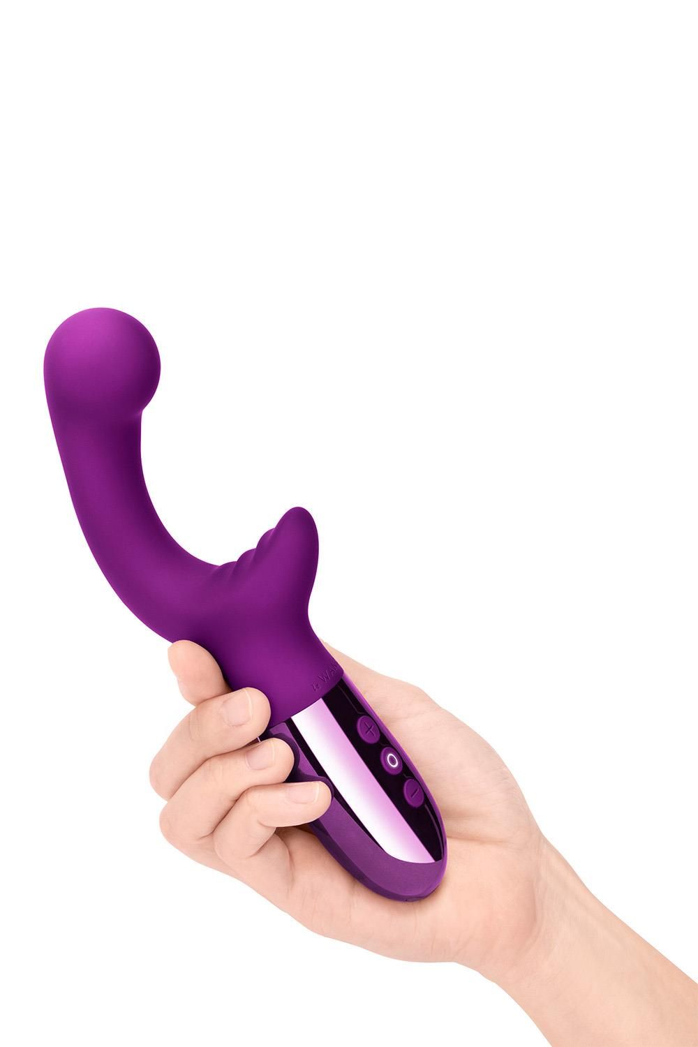 Hand hält lila Vibrator. Gebogene Form, silberfarbener Sockel mit drei Knöpfen. Oberteil mit abgerundeter Spitze.