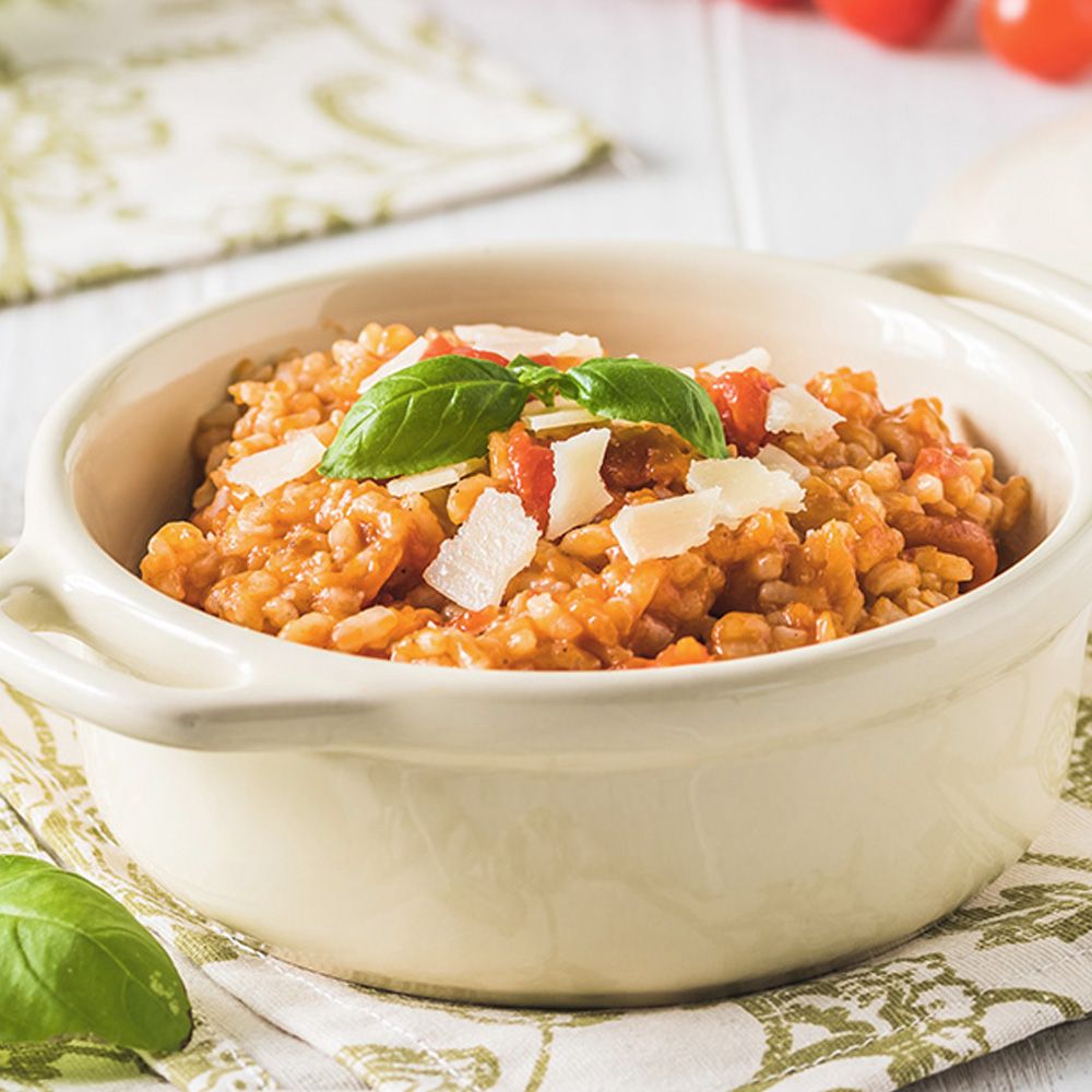 Tomaten-Risotto in einer cremefarbenen Schüssel, garniert mit Basilikumblättern und Käsespänen.