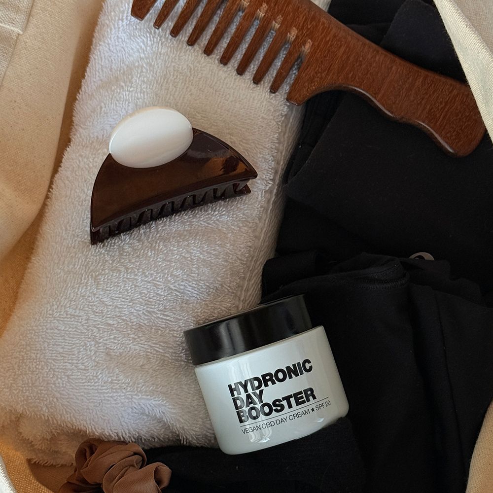 Tiegel mit Aufschrift: HYDRONIC DAY BOOSTER, Vegan CBD Day Cream + SPF 20, neben Haarklammer, Kamm und Handtuch.
