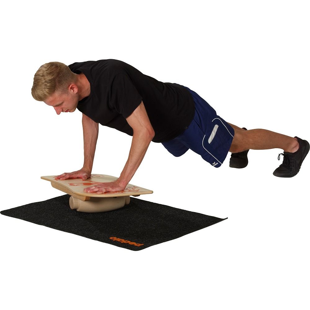 Mann macht Liegestütze auf einem Balance Board. Das Board liegt auf einer schwarzen Matte mit Logo.