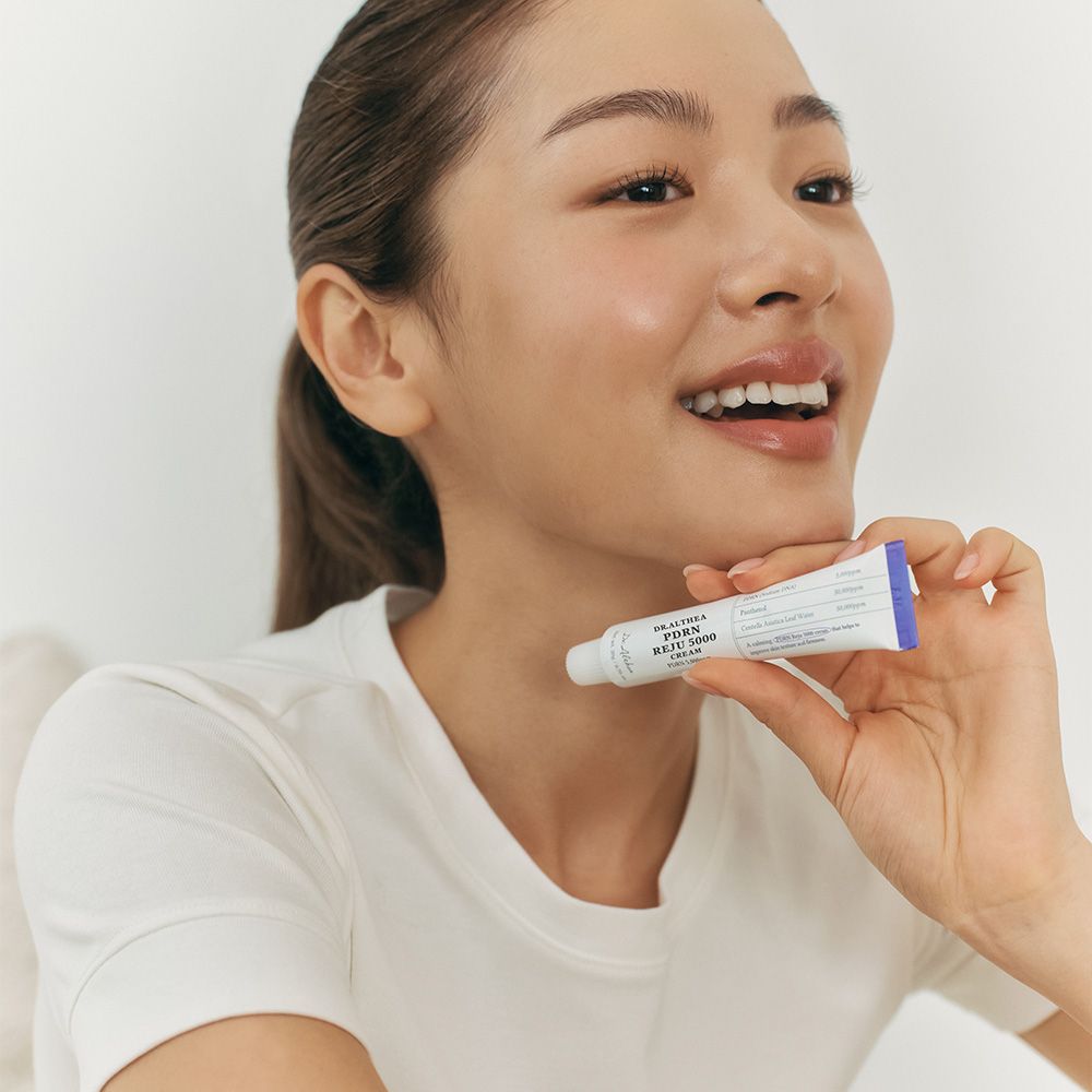 Frau hält eine Tube Dr.Althea PDRN Reju 5000 Cream an ihren Hals.