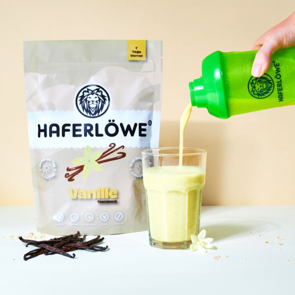 Vanille-Pulver von HAFERLÖWE wird in ein Glas gegossen. Vanilleschoten und eine Blüte liegen daneben. Grüner Shaker.