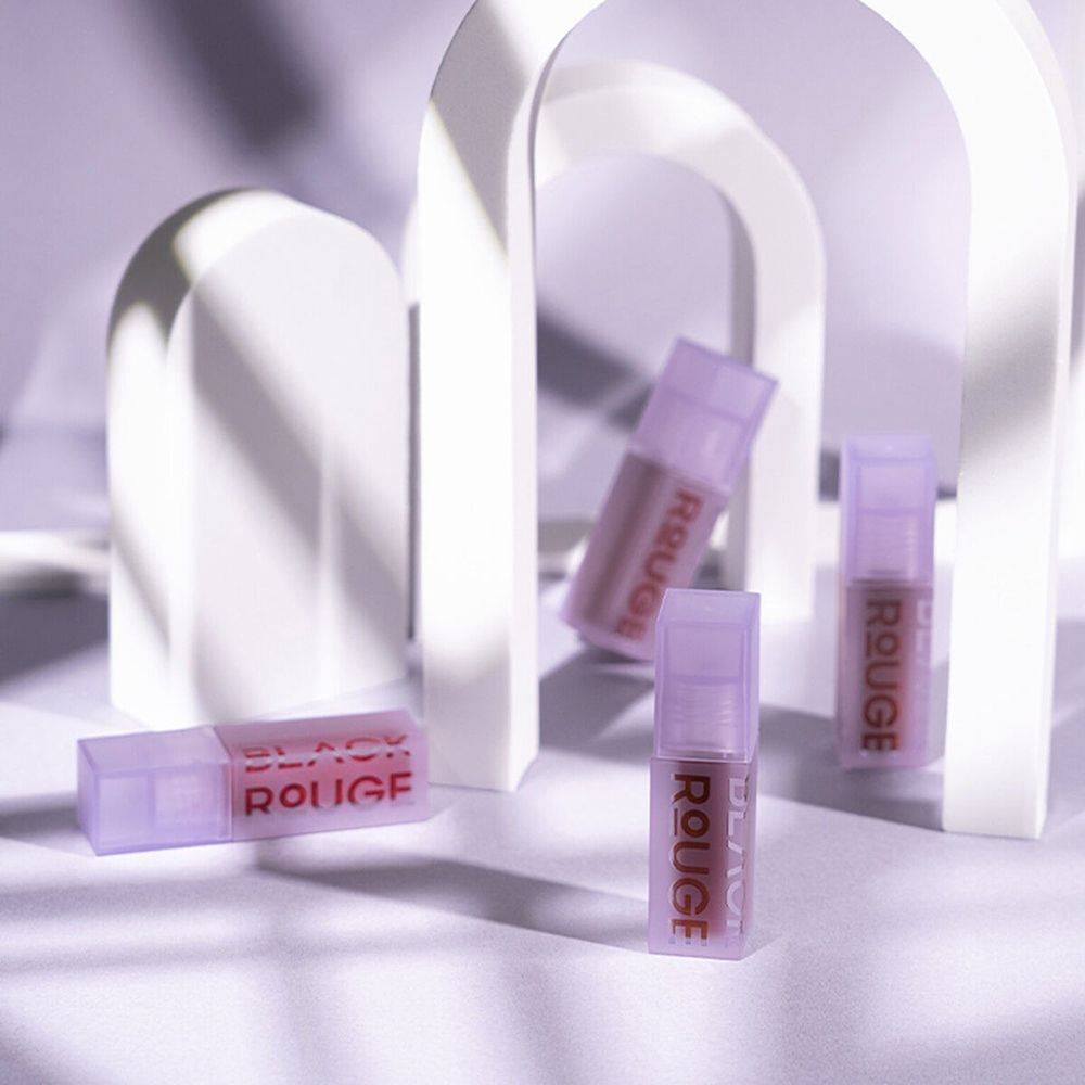 Mehrere Lipgloss-Flakons mit Deckel. Aufschrift BLACK ROUGE. Hintergrund: weiße Bögen.