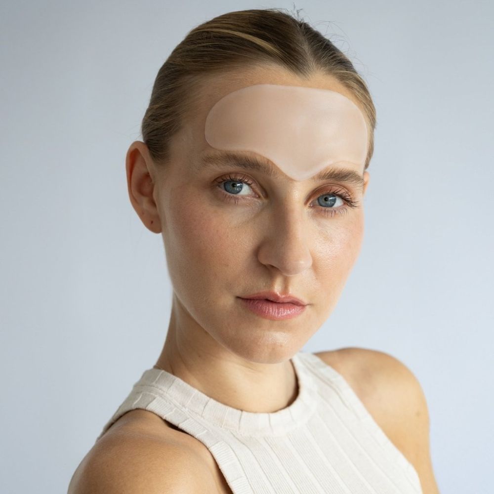 Eine Frau mit einem durchsichtigen Stirn Pad auf der Stirn. Das Pad bedeckt den Bereich zwischen den Augenbrauen.