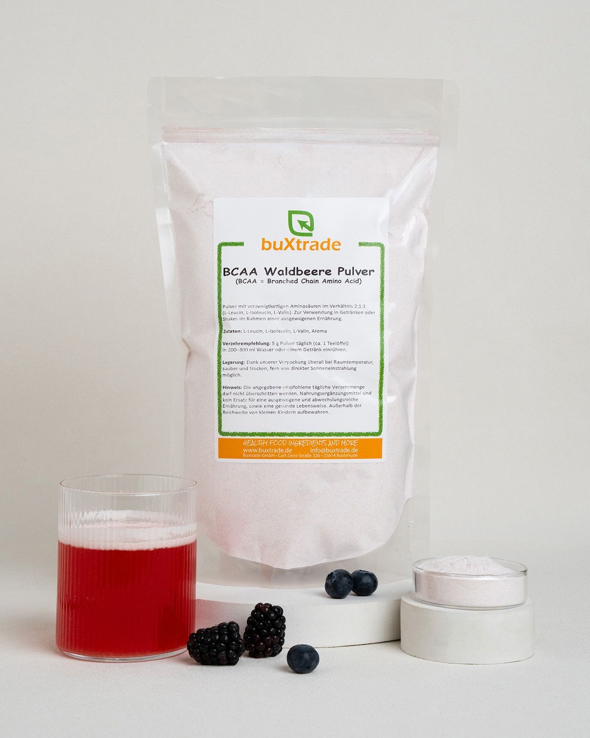 Pulververpackung neben einem Glas rotem Getränk, Beeren und einem kleinen Behälter mit Pulver.