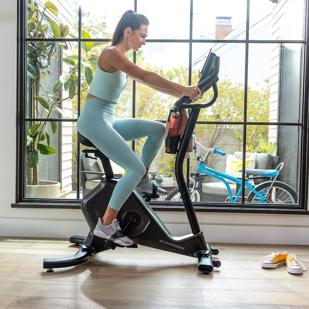 Fahrradtrainer Schwinn 590U. Schwarzer Rahmen, Frau trainiert. Wasserflasche am Rahmen. Schuhe am Boden.
