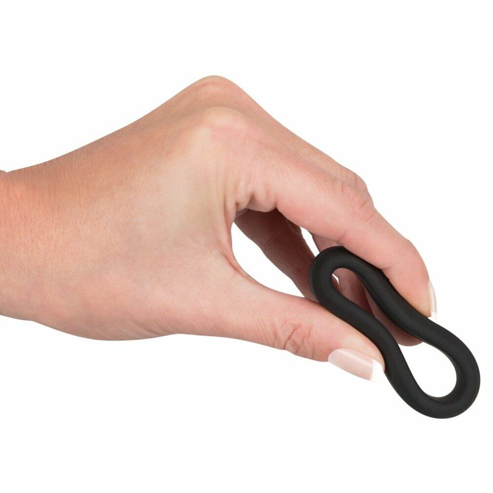 Hand hält schwarzen Penisring. Ring ist oval geformt und flexibel.