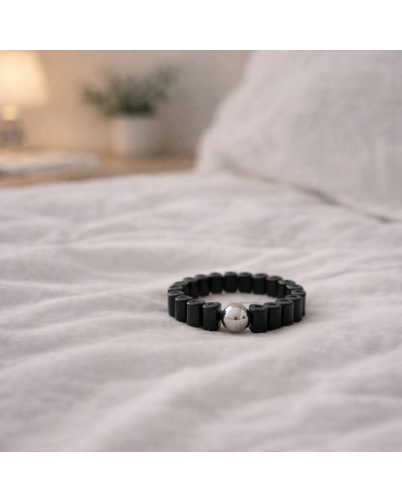 Schwarzer Ring mit silberner Kugel auf weißer Bettwäsche. Wellness-Produkt.