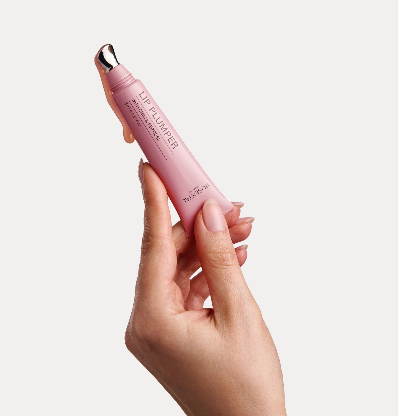 Hand hält rosa Tube. Aufschrift: LIP PLUMPER WITH CHILI & PEPTIDES. Marke: Rosental Organics. Applikator sichtbar.