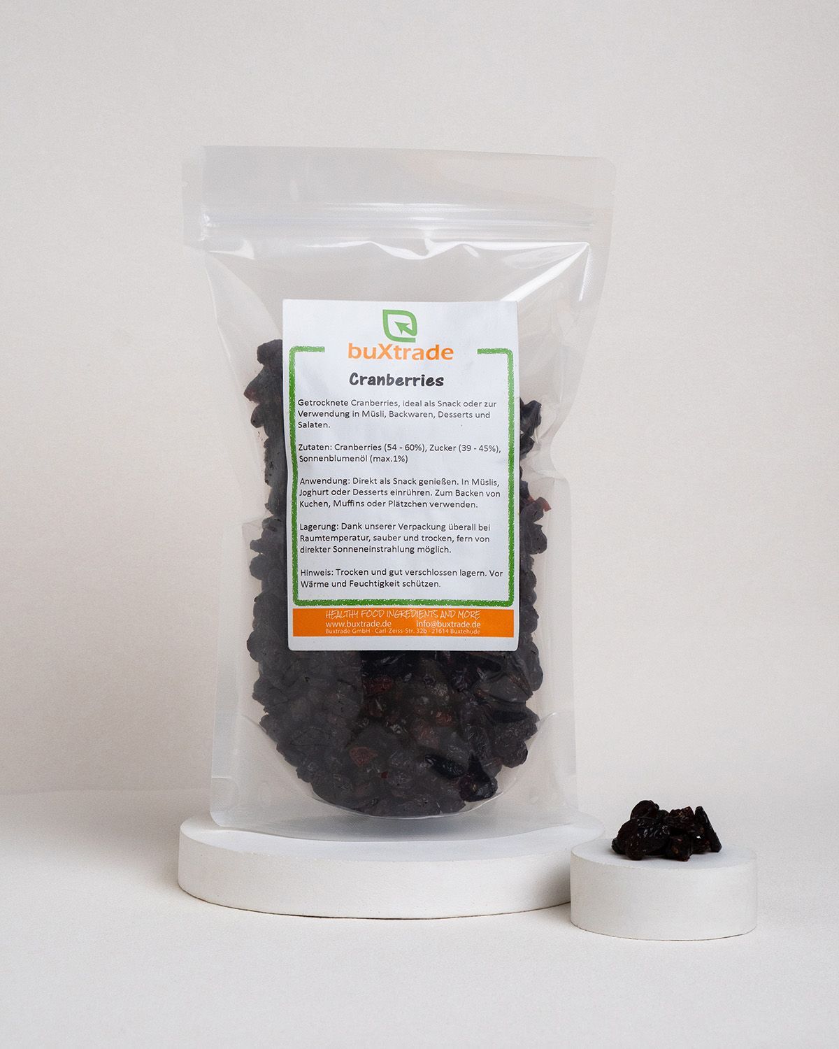 Transparente Verpackung mit Cranberries. Etikett: buXtrade Cranberries. Kleiner Podest mit Cranberries daneben.