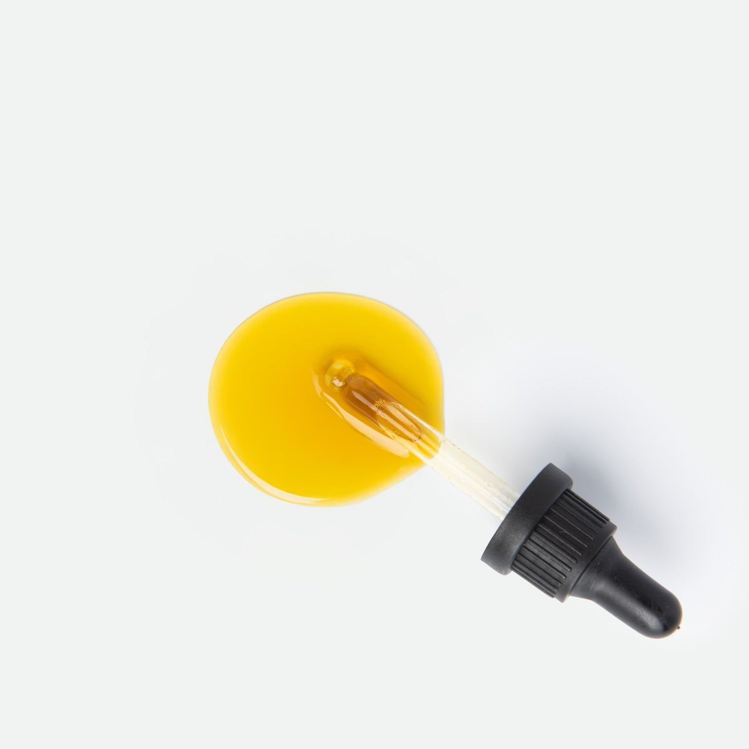 Tropfen gelbes CBD-Öl mit einer Pipette auf weißem Hintergrund.