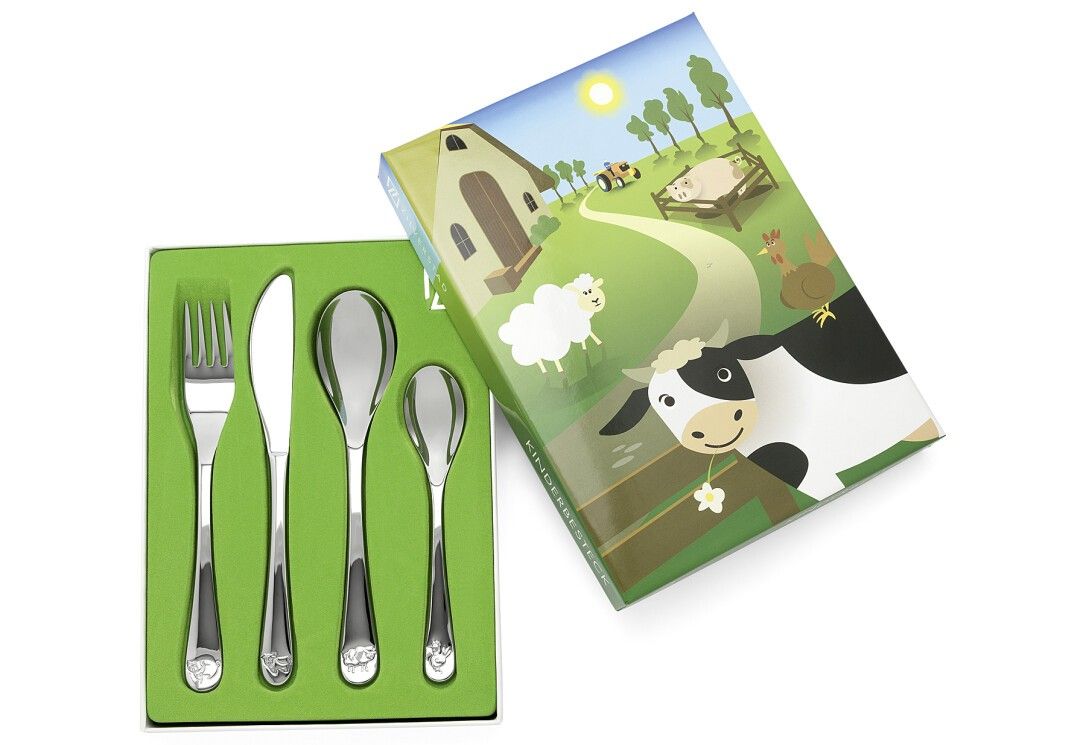 Vierteiliges Kinderbesteck in grüner Schachtel. Gabel, Messer, Löffel, Teelöffel. Verpackung mit Bauernhofmotiv. Glänzendes Metall.