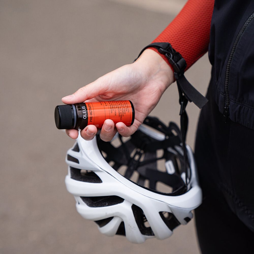 Hand hält eine Flasche OLEUS. Daneben ein Fahrradhelm. Roter Ärmel.