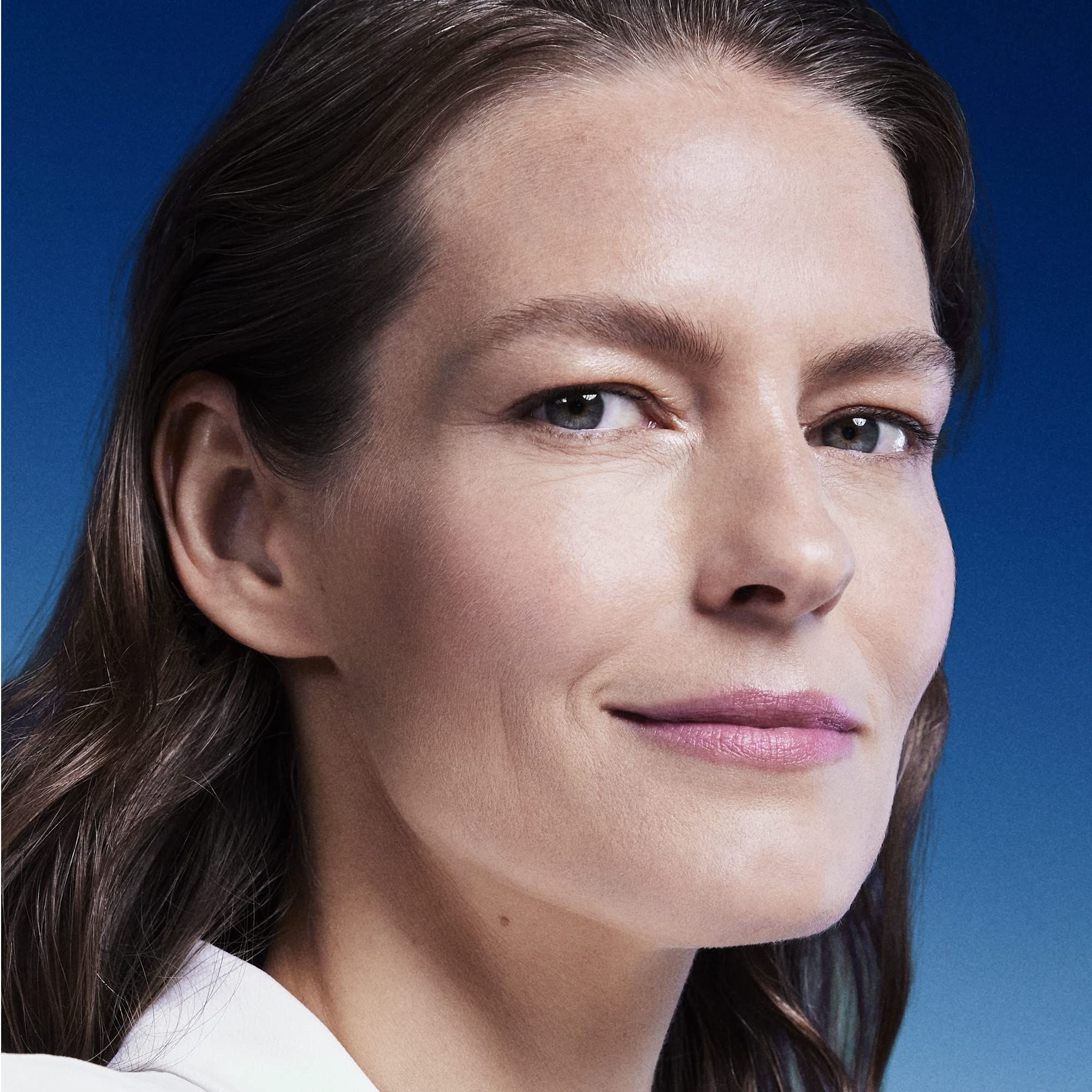 Porträt einer Frau mit braunen Haaren. Sie blickt in die Kamera und lächelt leicht. Blauer Hintergrund.