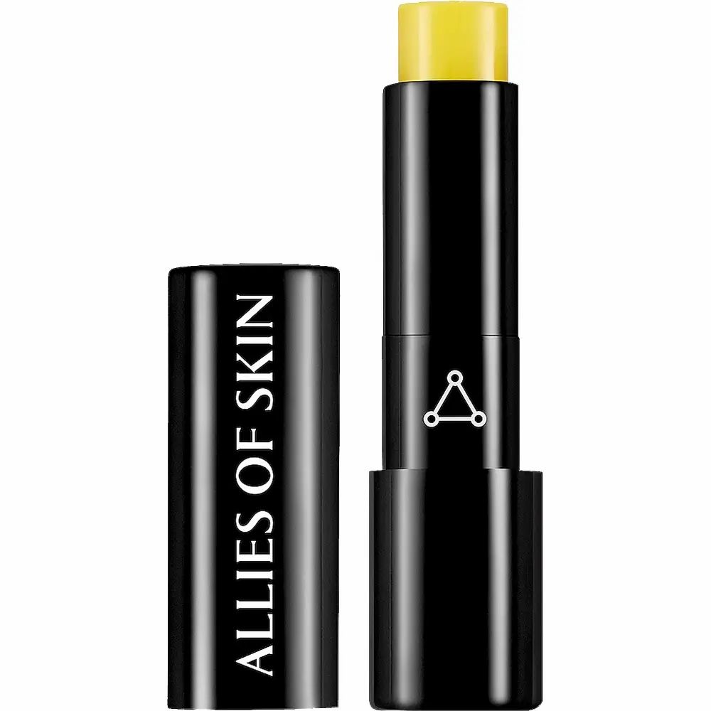 Schwarzer Lippenbalsam-Stick mit gelber Spitze. Deckel mit "ALLIES OF SKIN"-Schriftzug. Logo mit drei Punkten.