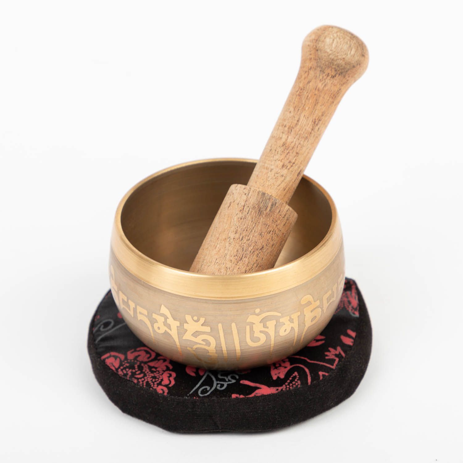 Klangschale mit Schriftzeichen, Holzschlägel, auf rotschwarzem Kissen. Goldfarbenes Metall, Holz. Auf weißem Hintergrund.