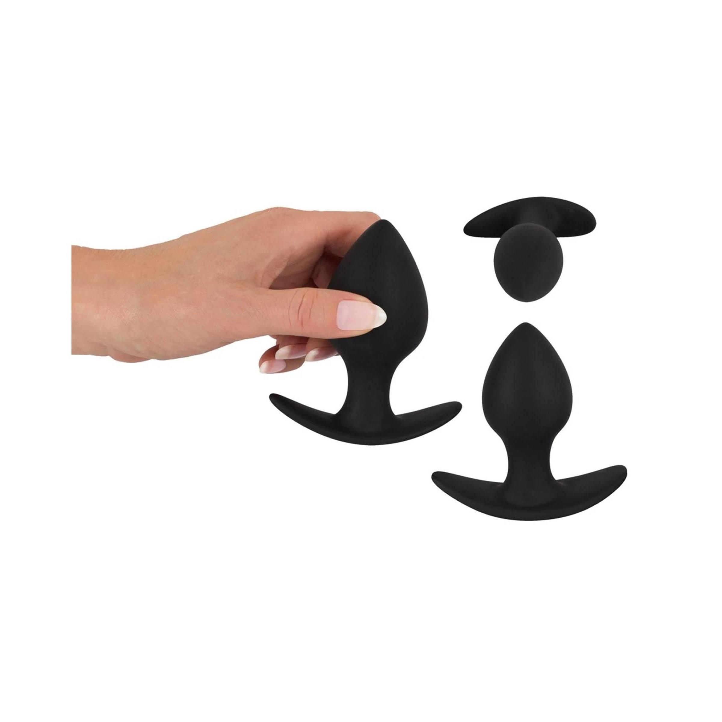 Hand hält zwei schwarze Anal-Trainer. Konische Spitze, gebogene Basis. Unterschiedliche Größen.