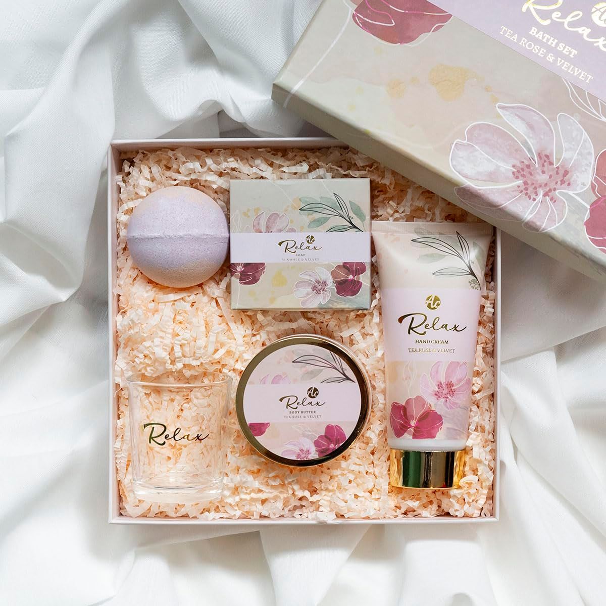 Geschenkbox mit Bade- und Pflegeprodukten. Enthält Handcreme, Glas, Seife, Badekugel und Creme. Auf weißem Stoff platziert.