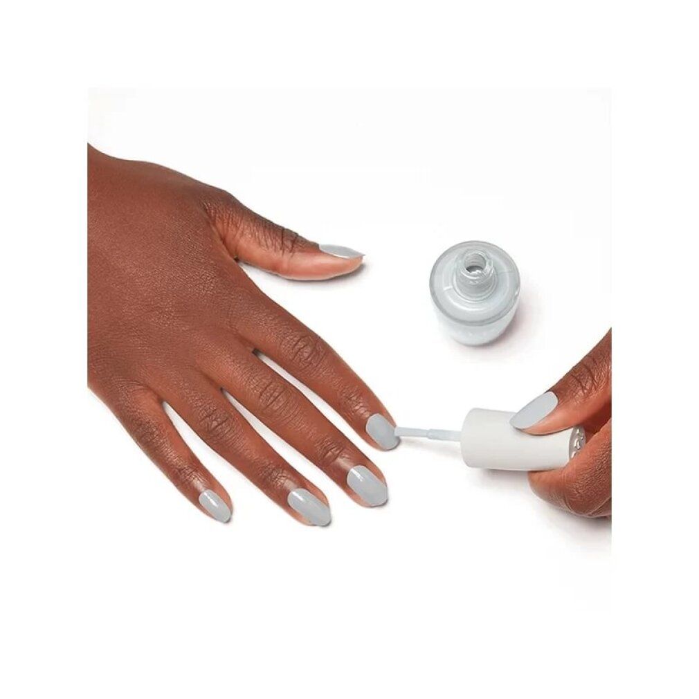 Nagellack in Hellgrau. Eine Hand mit lackierten Nägeln, eine weitere Hand lackiert einen Nagel. Flasche mit Nagellack.