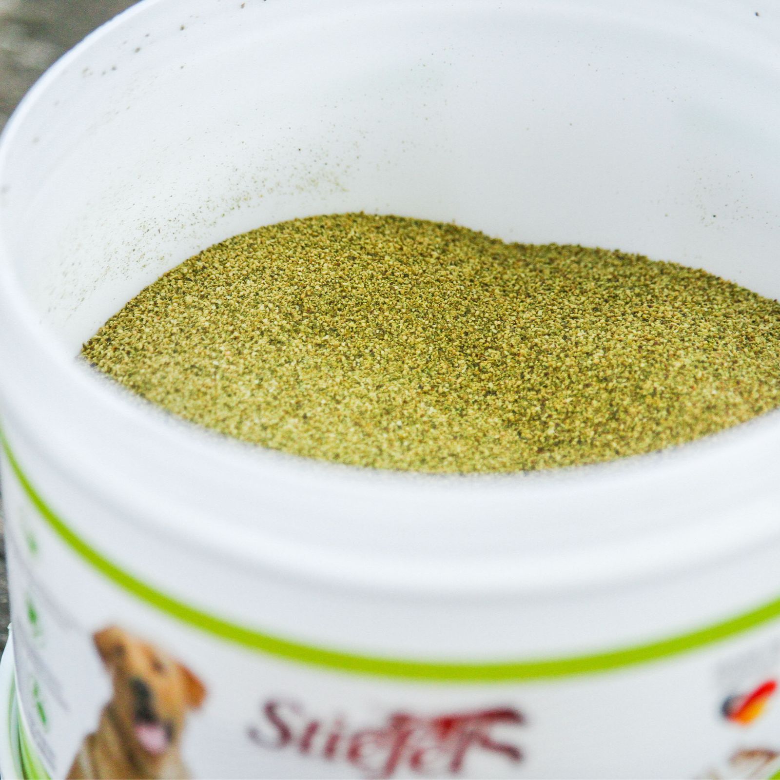 Weißer Eimer mit grünem, pulverförmigem Stiefel Seealgenmehl. Nahaufnahme, Produkt im Behälter.