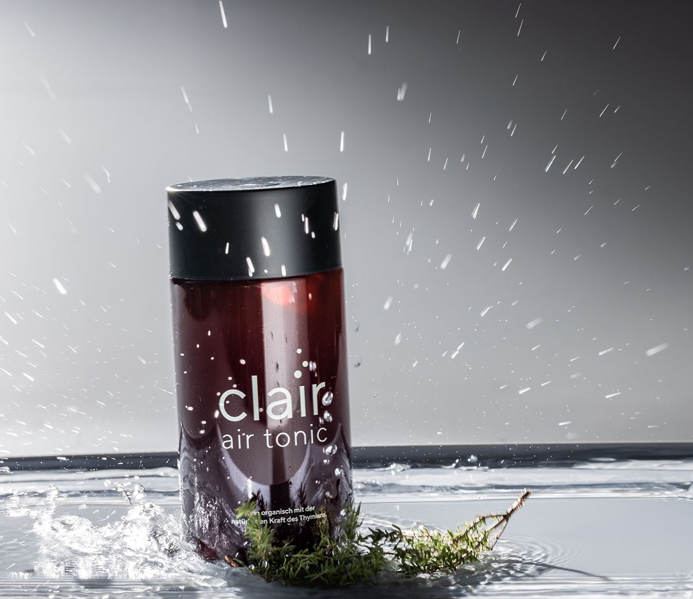Eine Flasche mit schwarzem Deckel und rotem Inhalt. Aufschrift: clair air tonic. Wasser spritzt.