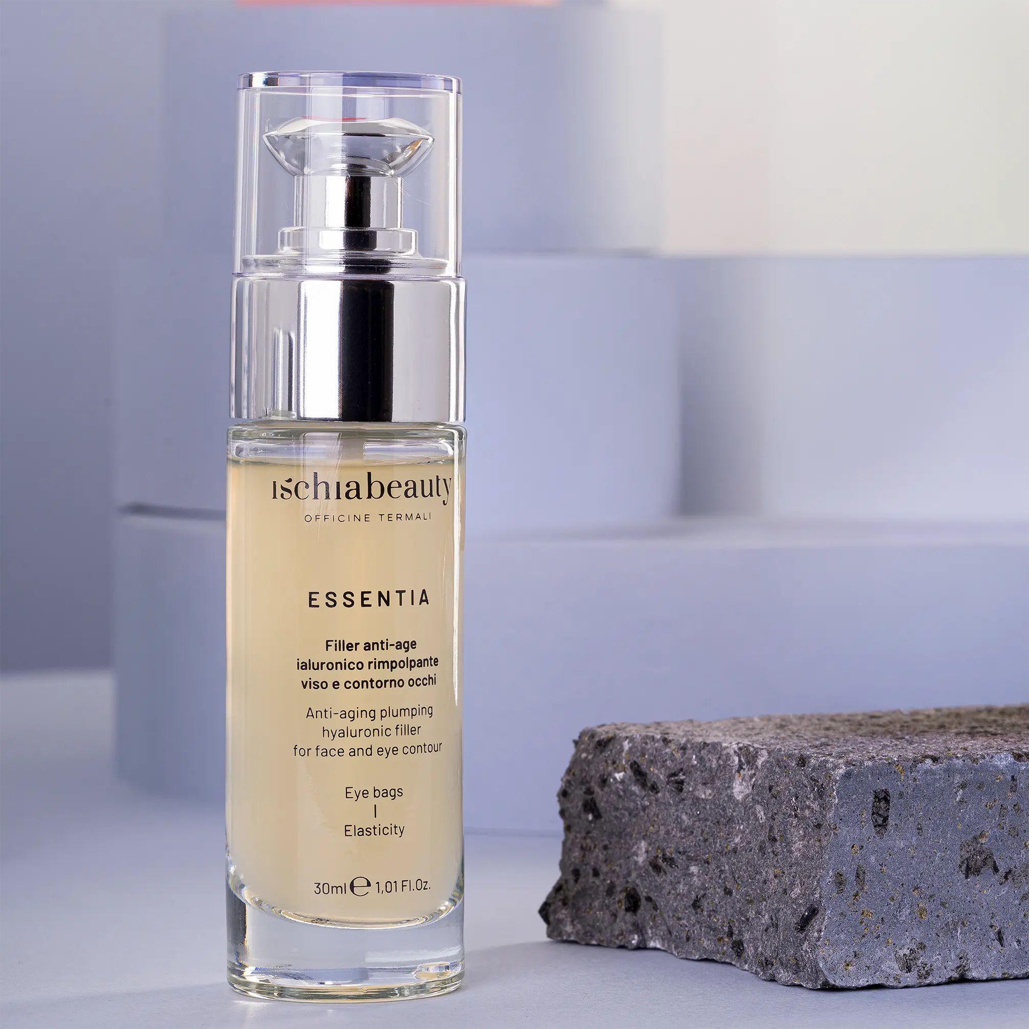 Glasflasche mit silberner Pumpe. Aufschrift: ischiabeauty, ESSENTIA, Filler anti-age, Augenringe, Elastizität. Auf grauem Stein.