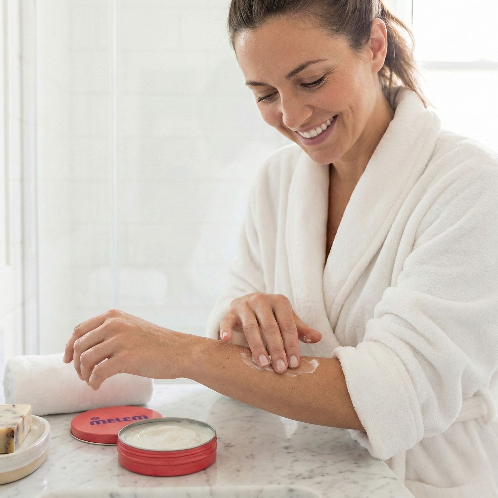 Frau trägt Creme auf den Arm auf. Roter Tiegel mit Produktlogo ist geöffnet.