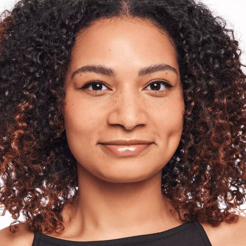 Porträt einer Frau mit lockigem Haar. Sie hat Sommersprossen und trägt Make-up. Der Hintergrund ist weiß.