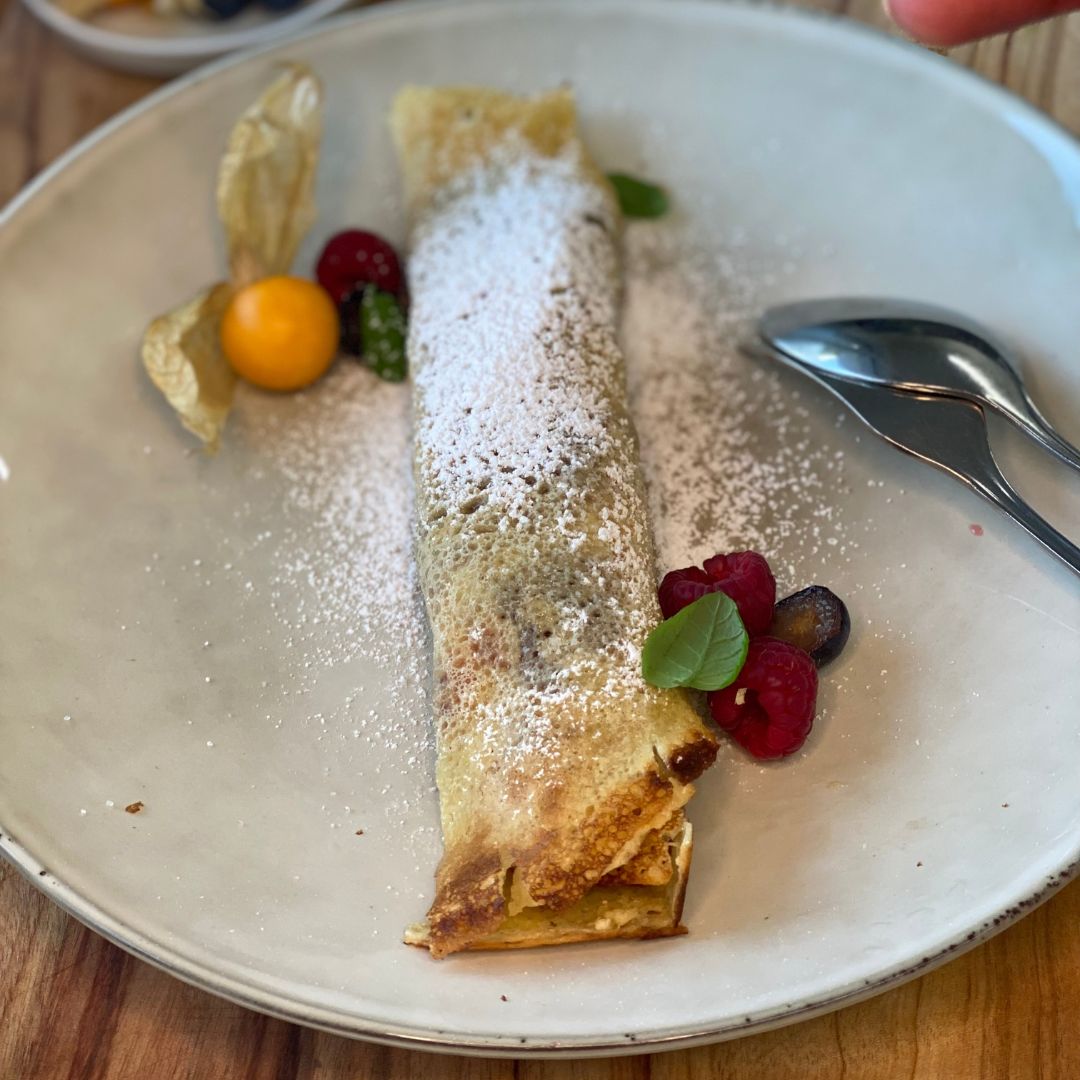 Gerollter Crêpe mit Puderzucker, Beeren und Physalis auf einem Teller.
