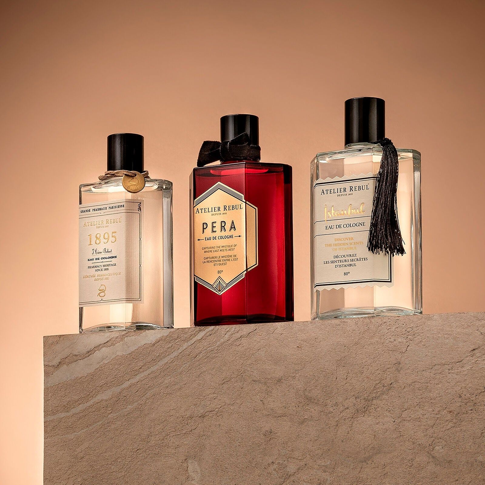 Drei Eau de Cologne Flaschen. Atelier Rebul Pera in Rot. Weitere Flaschen mit schwarzen Verschlüssen. Aufschrift sichtbar.