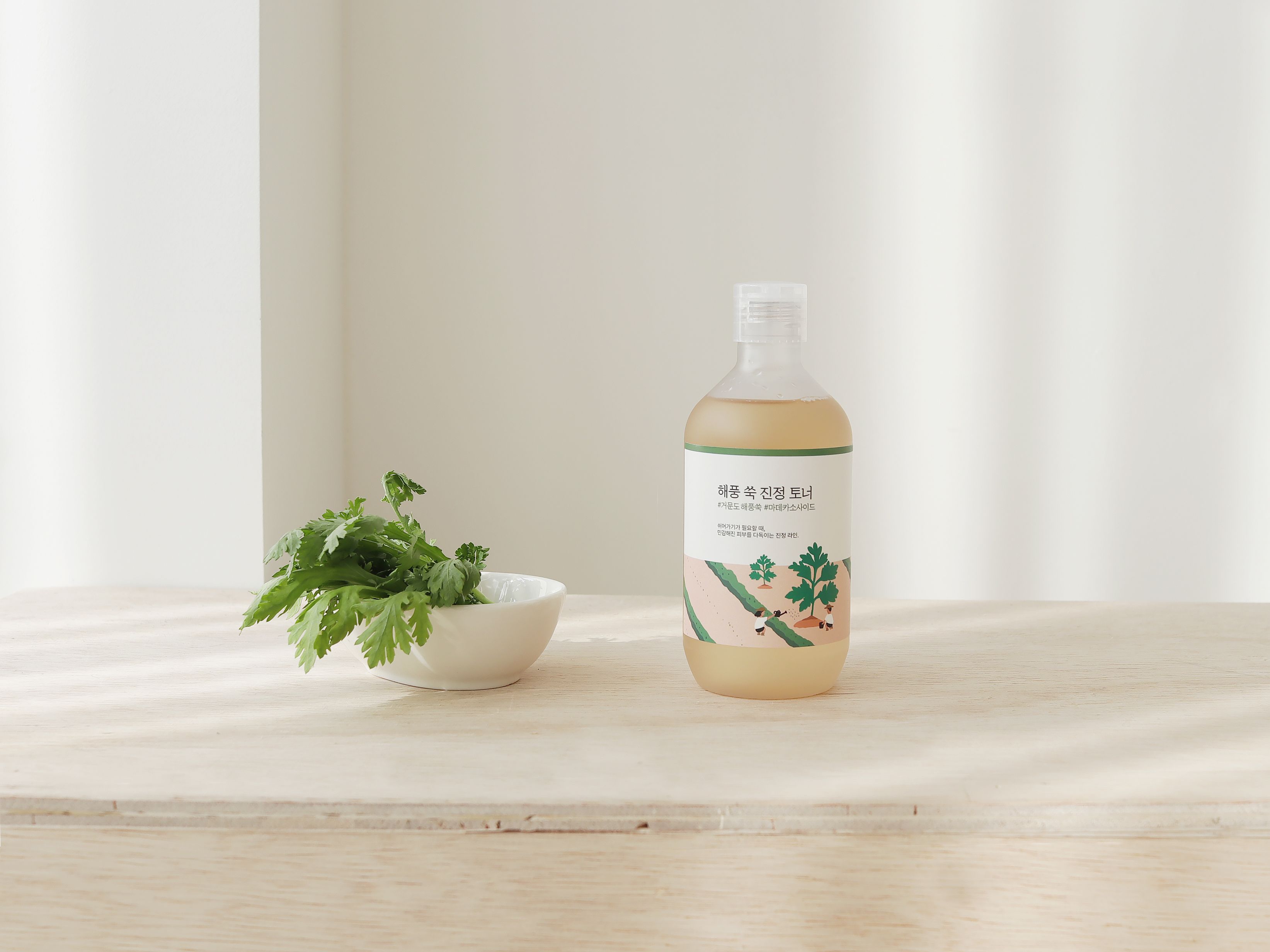Eine Flasche Toner steht auf einer Holzoberfläche neben einer Schale mit Kräutern. Der Hintergrund ist hell.
