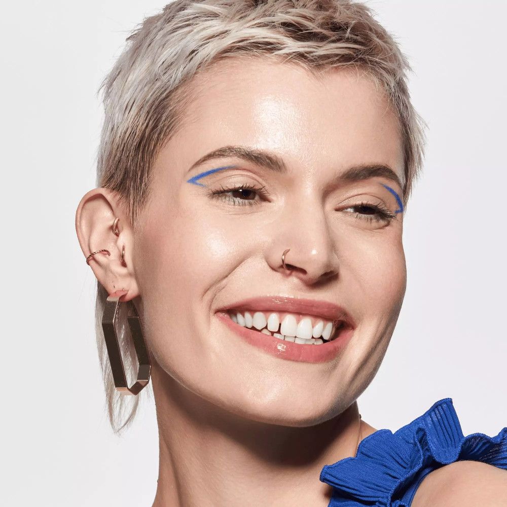 Porträt einer Frau mit Lippenstift. Sie lächelt. Blaue Lidstrich. Goldene Ohrringe.