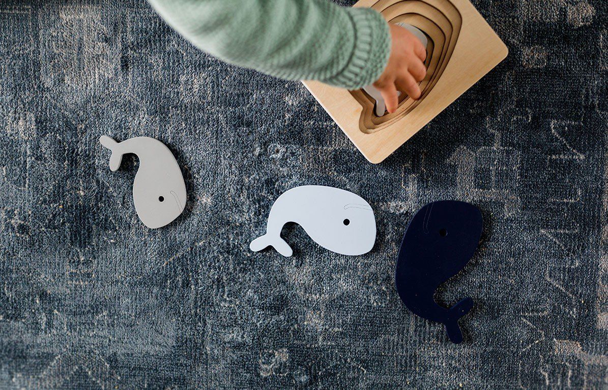 Kindsgut Wal-Puzzle mit Wal-Puzzleteilen. Mehrere Wal-Puzzleteile liegen neben dem Puzzle. Kind greift nach einem Teil.