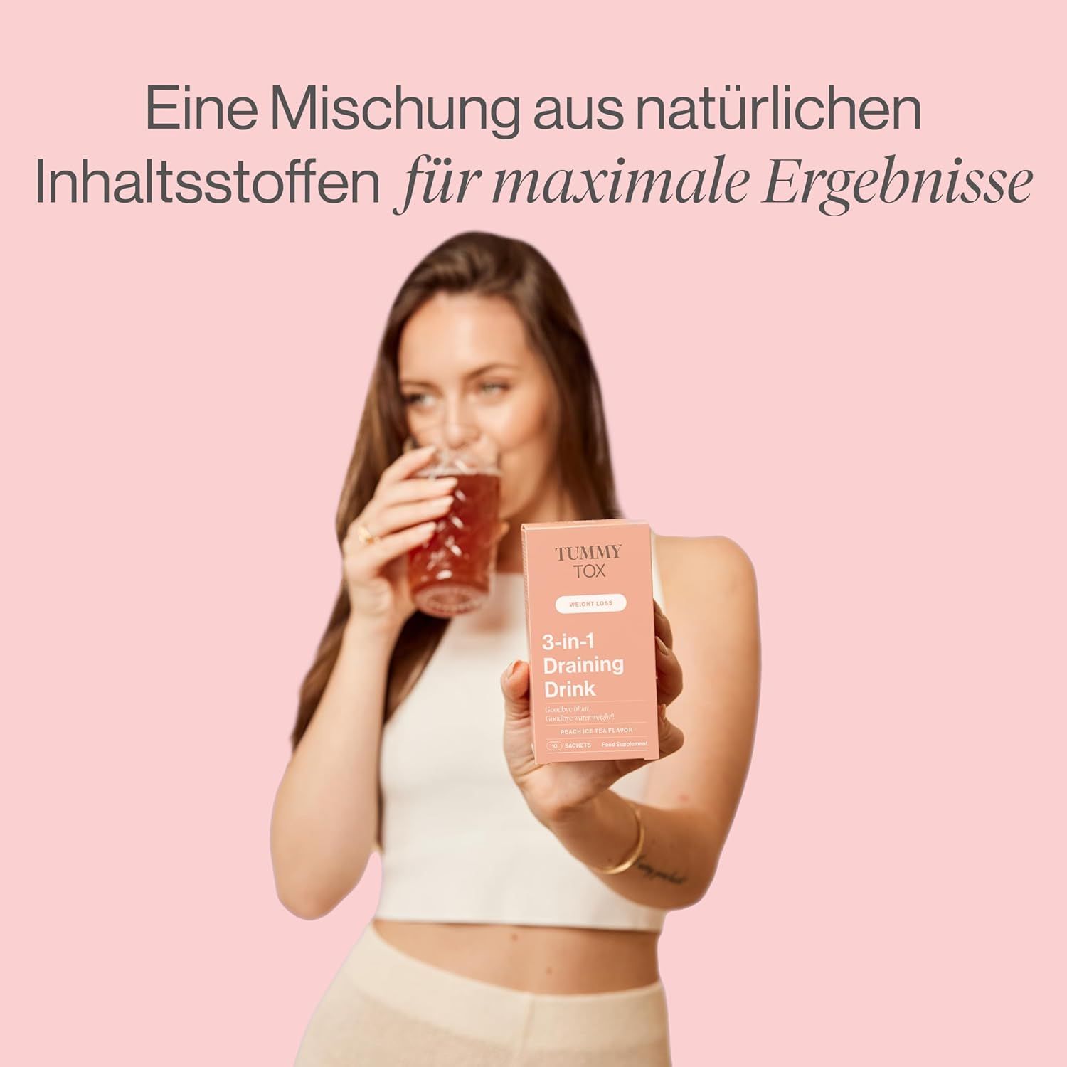 Frau trinkt ein Getränk aus einem Glas. Sie hält eine Packung "Tummy Tox 3-in-1 Draining Drink".