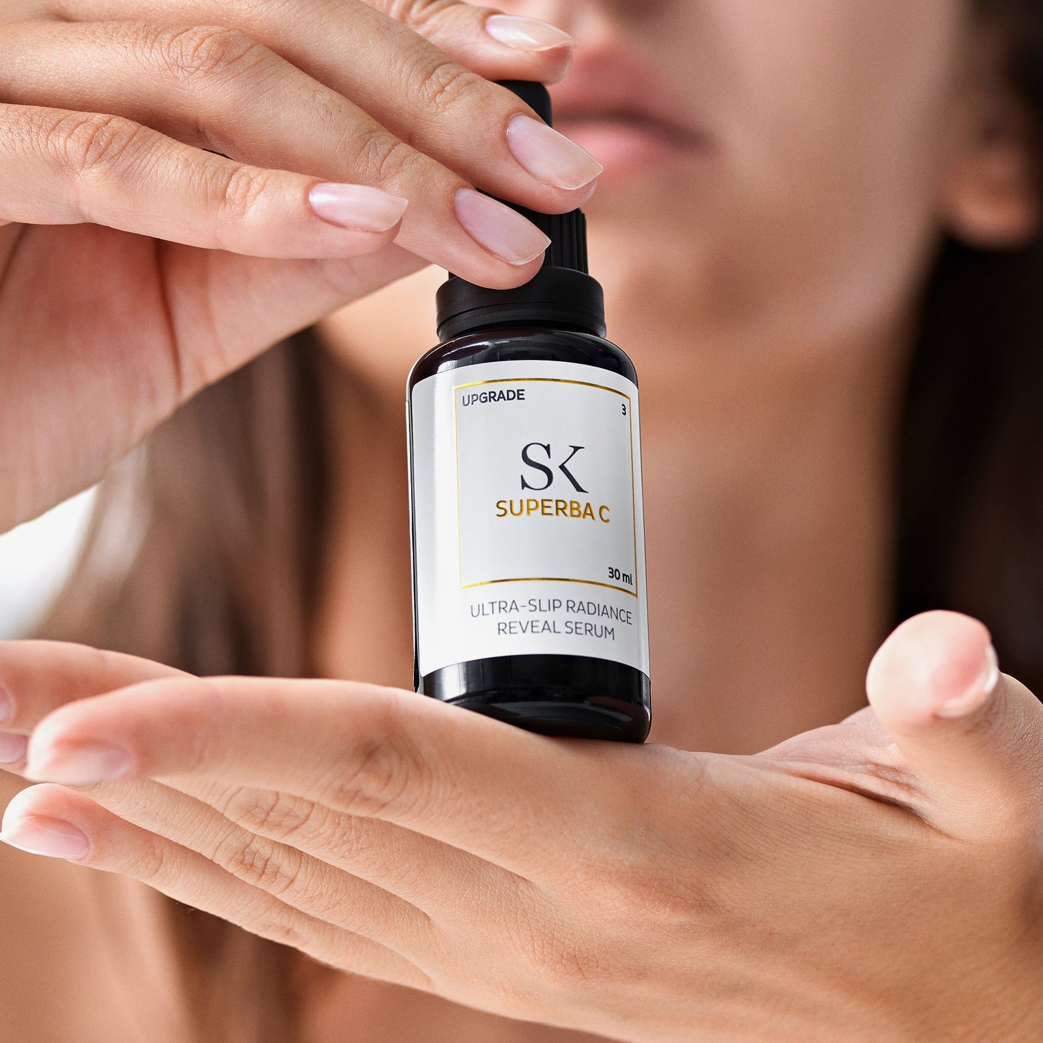 Hände halten eine schwarze Flasche mit Pipette. Auf dem Etikett steht "SK Superba C" und "Ultra-Slip Radiance Reveal Serum".